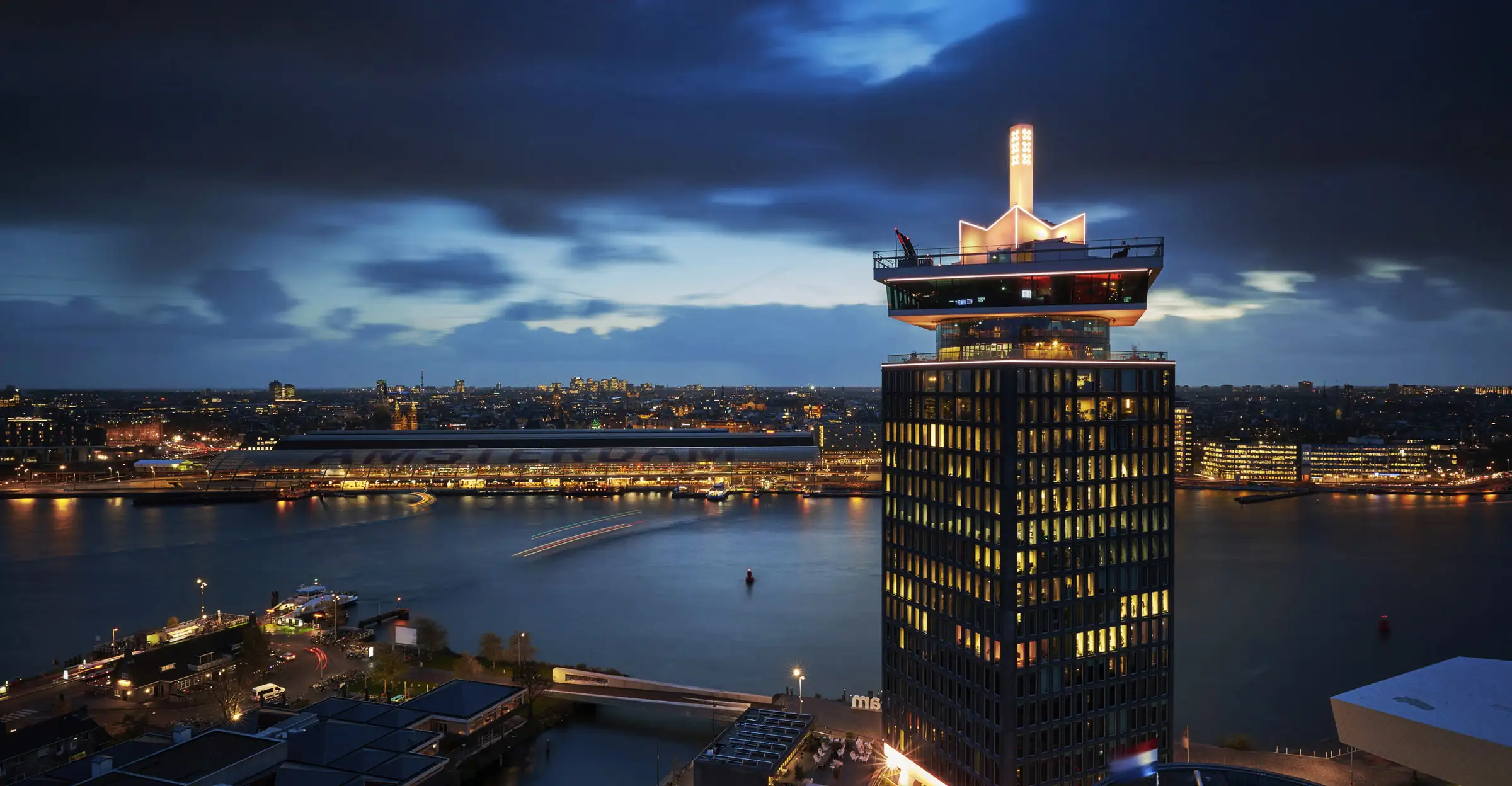 De A’DAM Toren bij avond, met het IJ en Amsterdam Centraal op de achtergrond